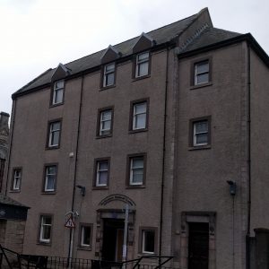 Colour photo of four-storey stone building, identified in an arched sign over the front door as the 'Nethergate Medical Centre'. Photo taken in low light.